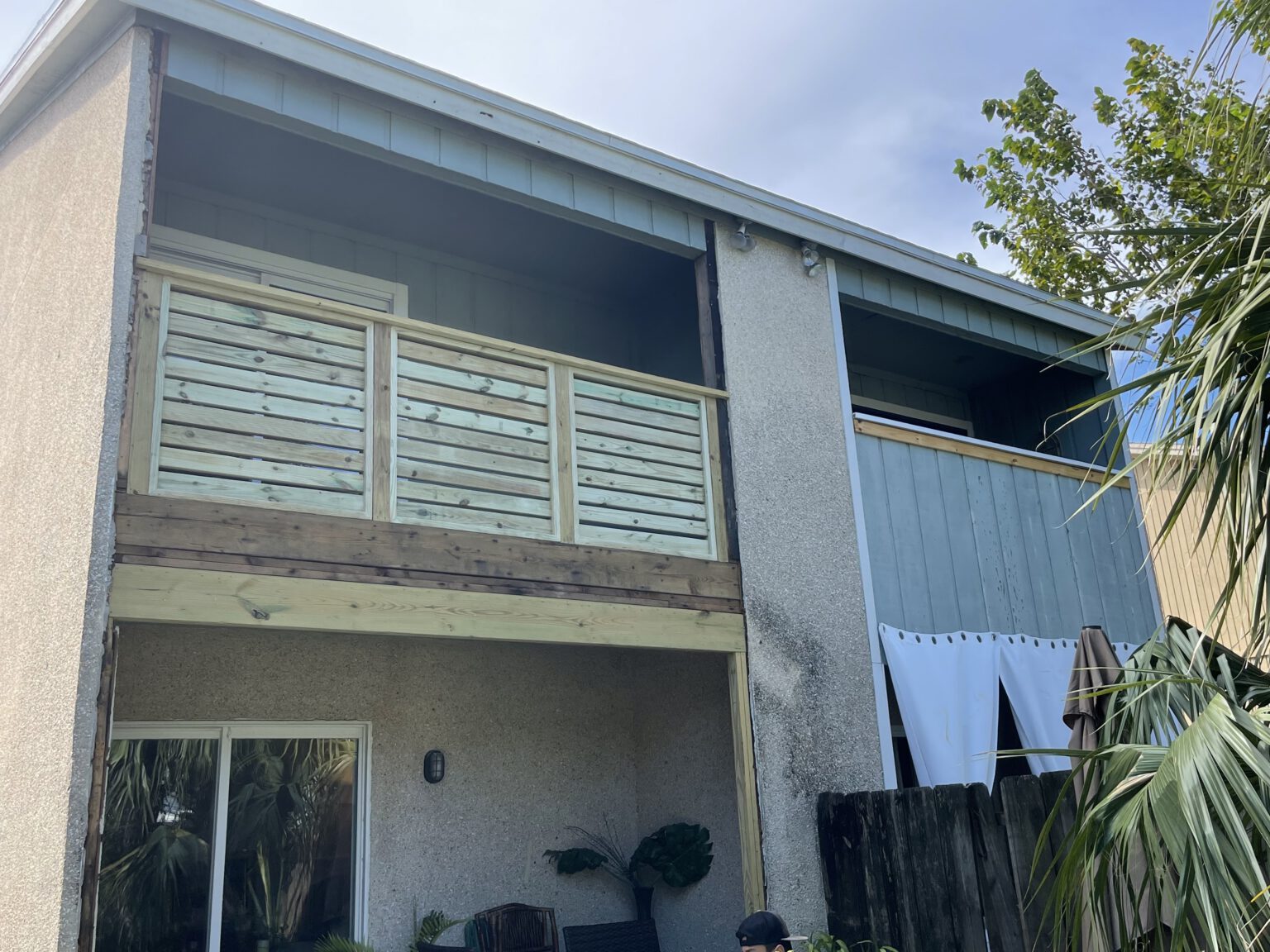 Two story beach home with rebuilt balcony framing and horizontal slat railing